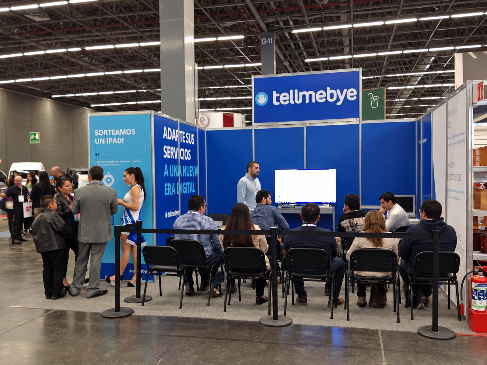 Estand de Tellmebye en la feria de Guadalajara, México, con visitantes sentados alrededor de la pantalla del primer velatorio digital.